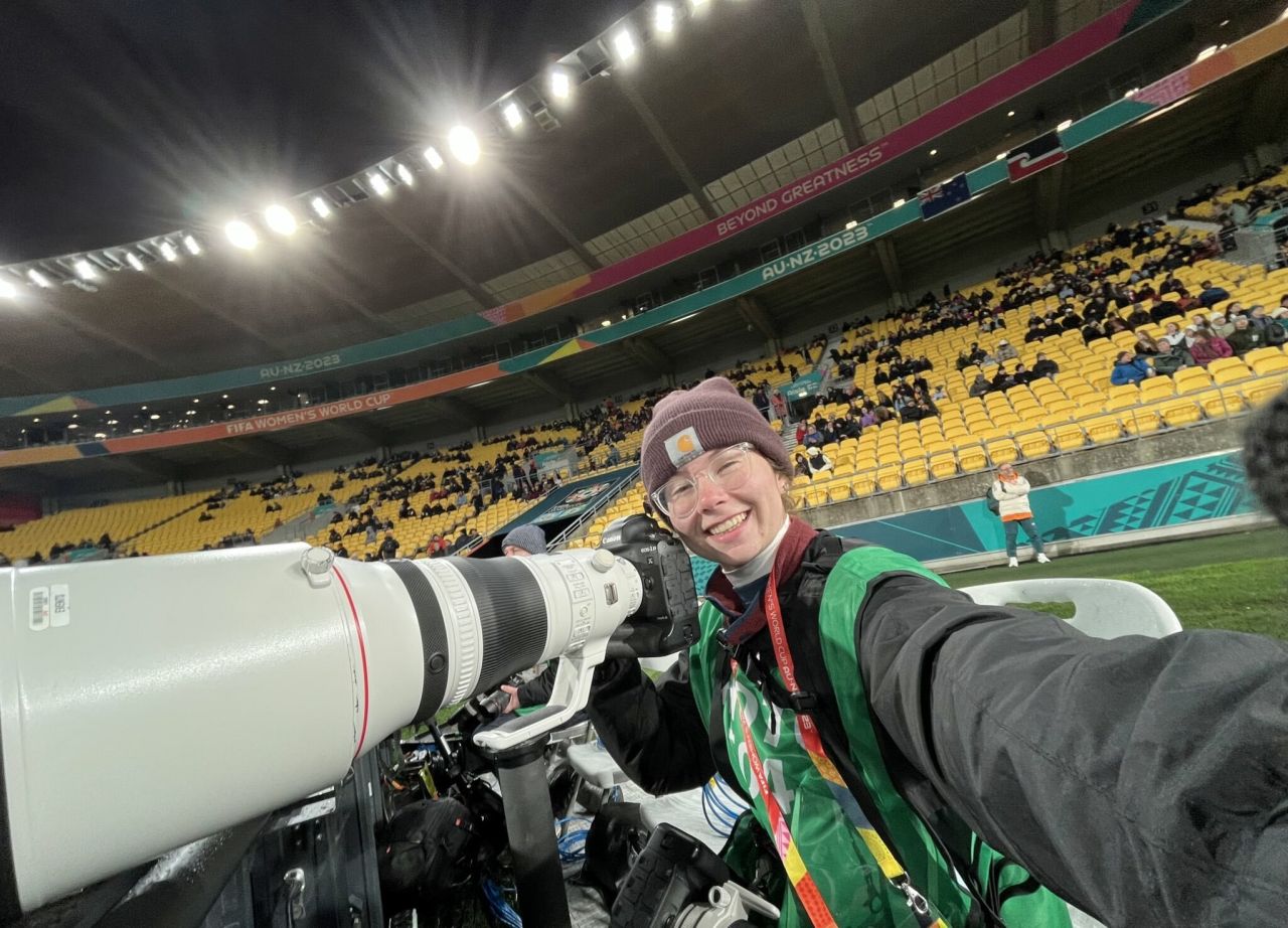 College student in a carhartt beanie cap with a long lens camera poses in an empty stadium after a world cup soccer match in New Zealand