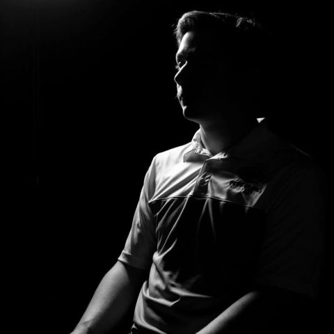 Male student posing in shadows on a black background to hide his identity