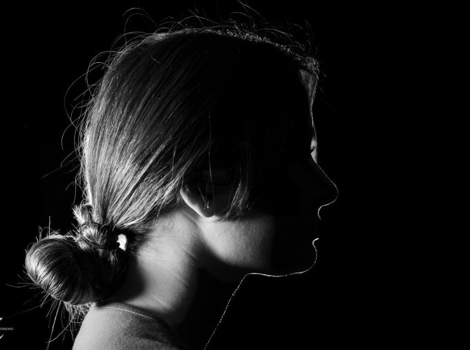Dark silhouette of a young female student with hair pulled back and her face in shadows to hide her identity