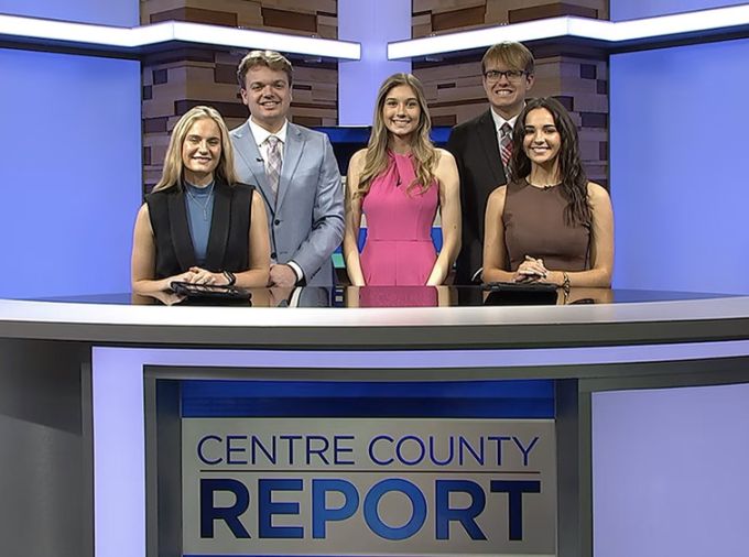 Five student broadcasters pose behind the reporting desk for Centre County Report