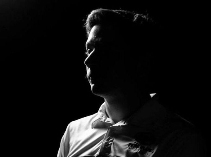 Male student posing in shadows on a black background to hide his identity