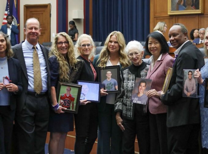 Eleven people pose in a court room holding photos of children they lost to hazing incidents