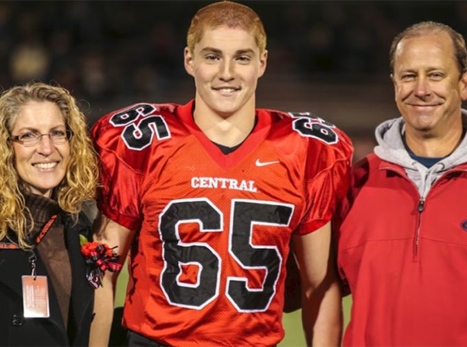 Tim Piazza, in a football uniform, stands between his mother and father for a senior night photo