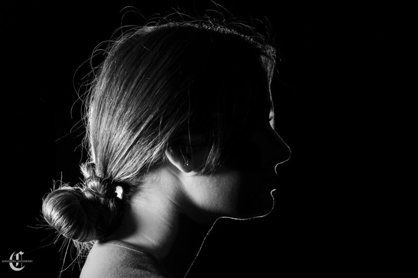 Dark silhouette of a young female student with hair pulled back and her face in shadows to hide her identity