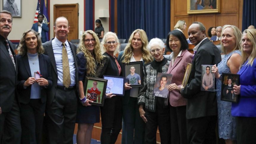 Eleven people pose in a court room holding photos of children they lost to hazing incidents